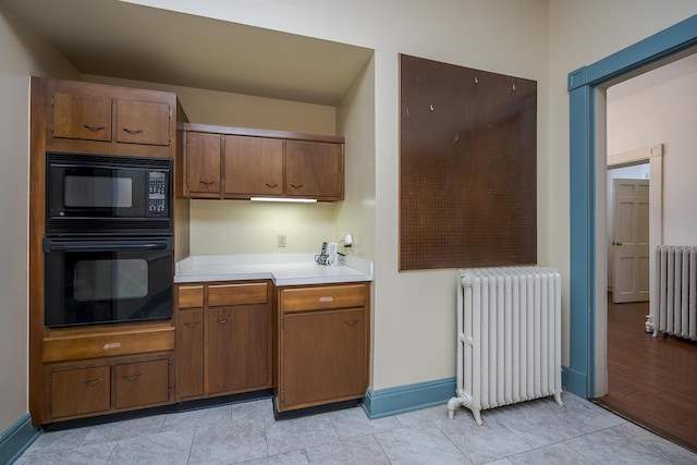 kitchen with black appliances, brown cabinetry, radiator heating unit, and light countertops