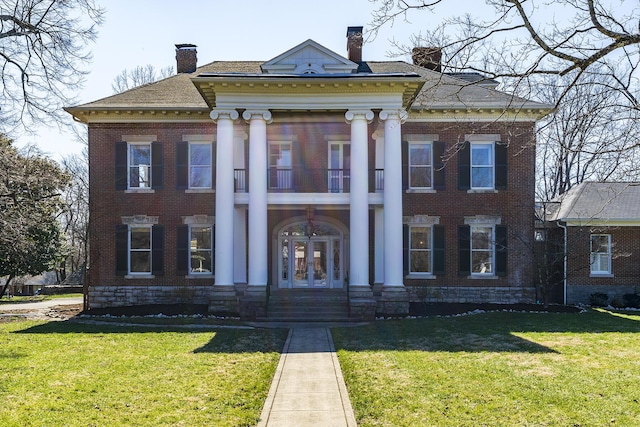 greek revival inspired property with brick siding, a front lawn, french doors, a chimney, and a balcony