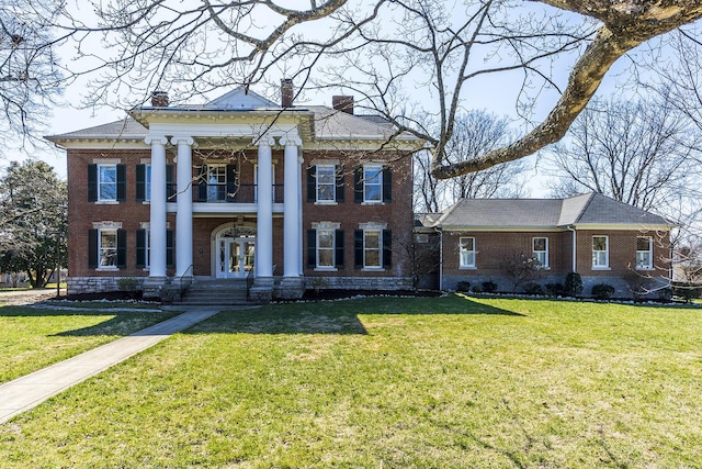 greek revival inspired property with a balcony, french doors, brick siding, and a chimney