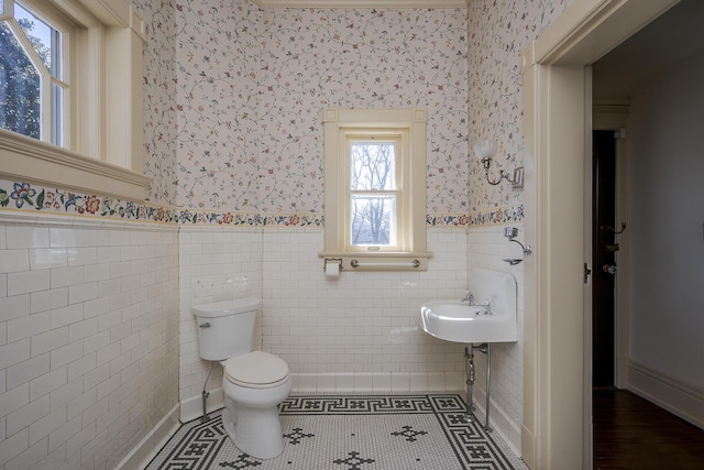 half bathroom with tile patterned flooring, wainscoting, wallpapered walls, and toilet