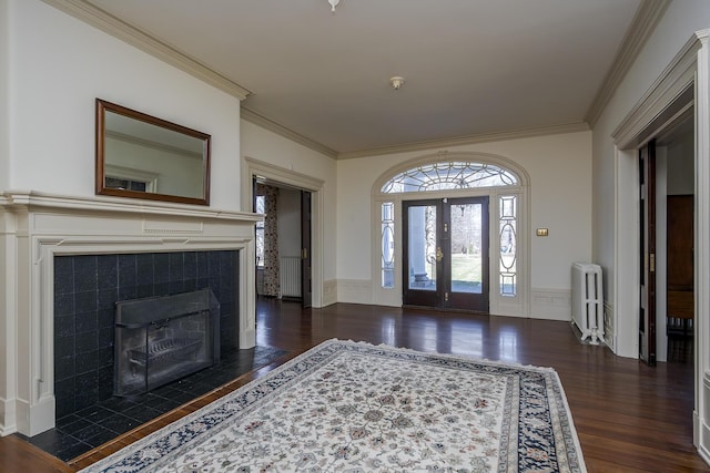 entryway with a wainscoted wall, a tiled fireplace, wood finished floors, radiator, and crown molding