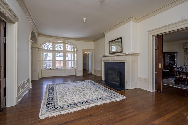 living area with a fireplace with flush hearth, ornamental molding, wainscoting, wood finished floors, and a decorative wall