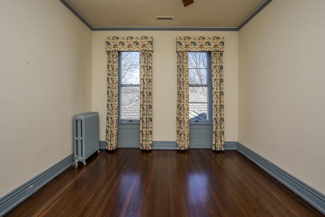 empty room featuring hardwood / wood-style floors, crown molding, radiator heating unit, and visible vents