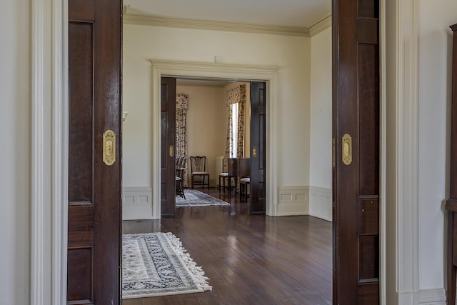 interior space with crown molding, a decorative wall, dark wood-style flooring, and wainscoting