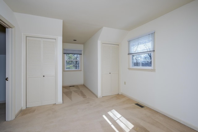 unfurnished bedroom with visible vents, multiple windows, two closets, and light colored carpet