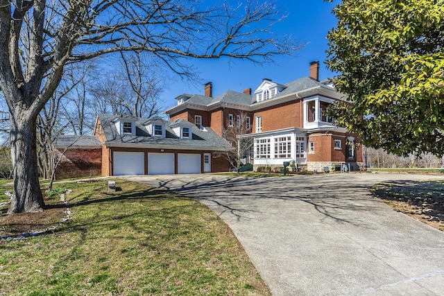 view of front of property featuring a chimney, a front lawn, a garage, aphalt driveway, and brick siding