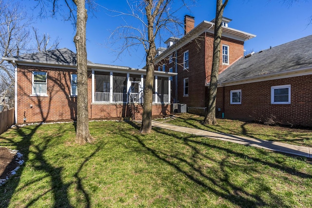 rear view of house featuring a yard, central AC, a sunroom, a chimney, and brick siding