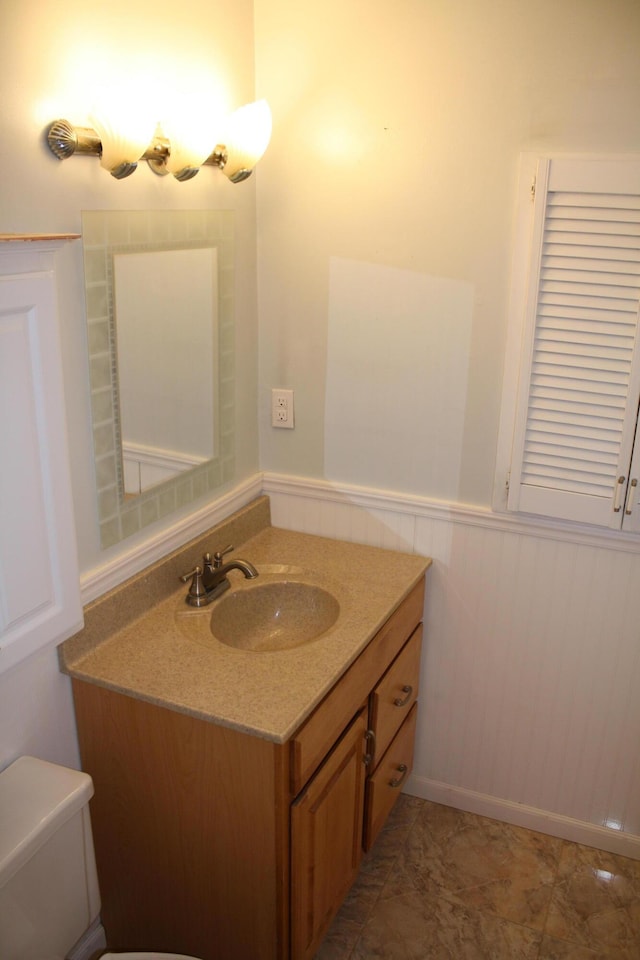 half bath with vanity, toilet, and wainscoting