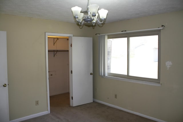 unfurnished bedroom with a walk in closet, a closet, an inviting chandelier, carpet flooring, and baseboards