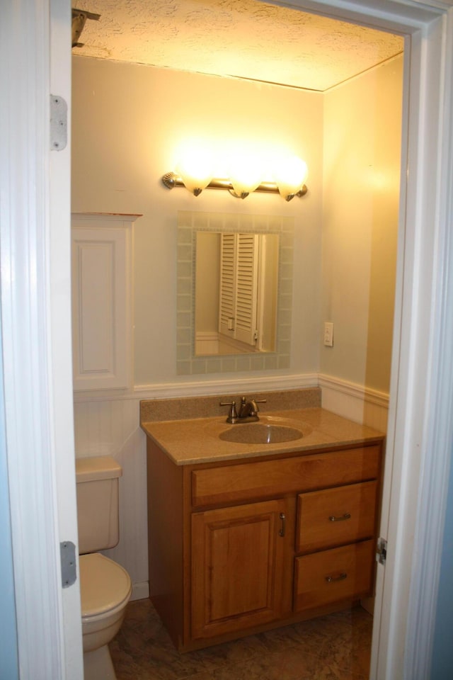 bathroom featuring vanity, toilet, and a wainscoted wall