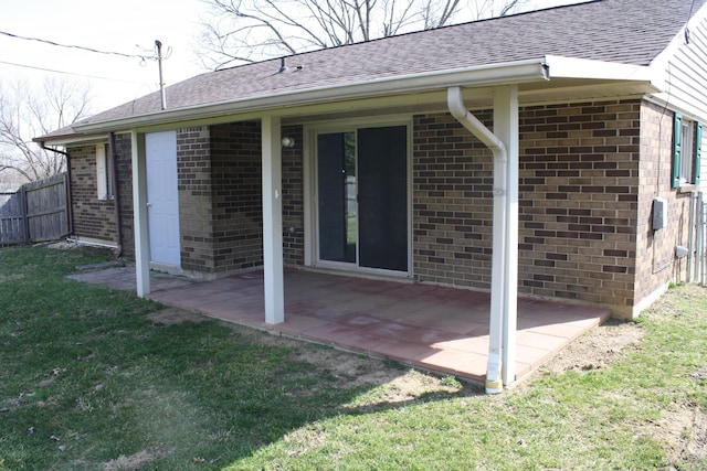 back of house featuring fence, roof with shingles, a yard, a patio area, and brick siding