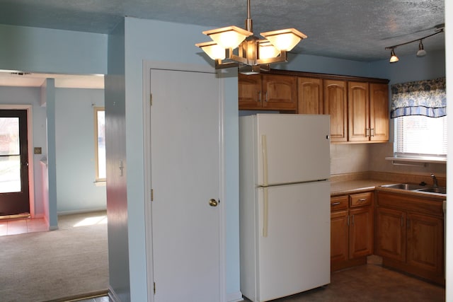 kitchen featuring dark colored carpet, brown cabinets, freestanding refrigerator, and a sink