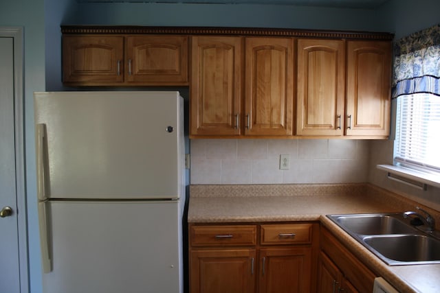 kitchen with freestanding refrigerator, a sink, light countertops, dishwasher, and brown cabinets