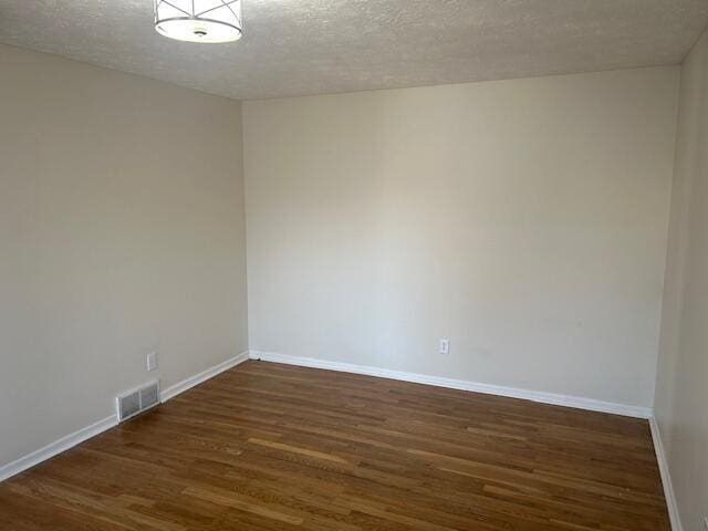 unfurnished room featuring visible vents, baseboards, a textured ceiling, and dark wood-style flooring