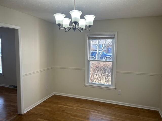 unfurnished dining area with baseboards, a textured ceiling, an inviting chandelier, and wood finished floors