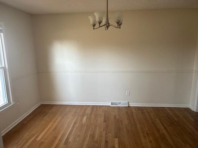 unfurnished dining area featuring visible vents, baseboards, an inviting chandelier, and wood finished floors