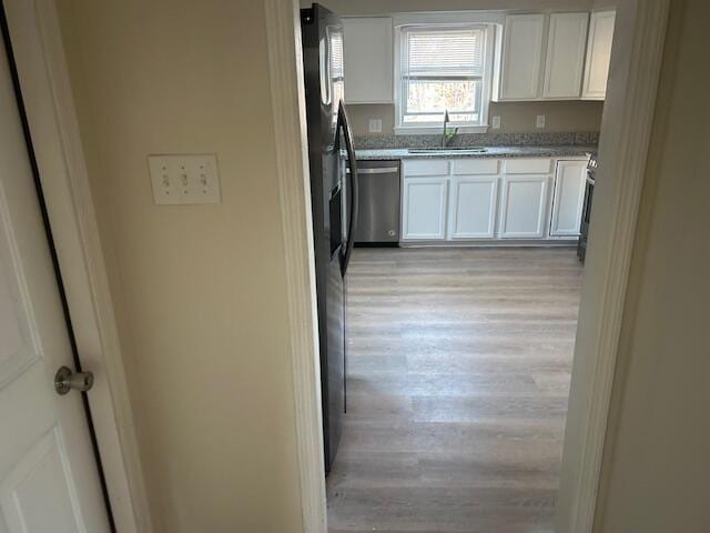 kitchen featuring light wood finished floors, stainless steel dishwasher, black refrigerator with ice dispenser, white cabinets, and a sink