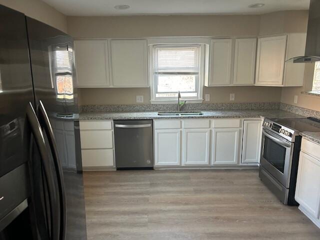 kitchen featuring wall chimney range hood, a wealth of natural light, stainless steel appliances, white cabinetry, and a sink