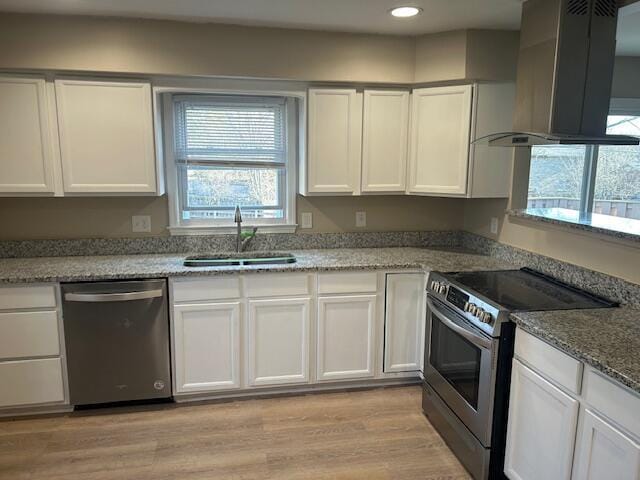 kitchen featuring light wood-type flooring, stainless steel appliances, exhaust hood, white cabinetry, and a sink