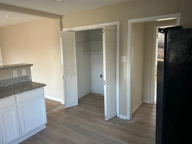 interior space with light wood-type flooring, stone countertops, white cabinetry, freestanding refrigerator, and baseboards