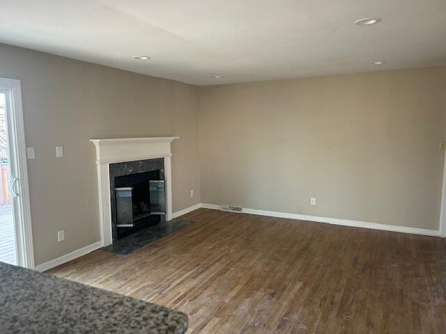 unfurnished living room with a premium fireplace, baseboards, visible vents, and wood finished floors