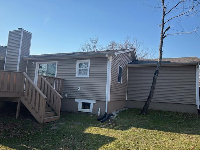 rear view of property featuring stairway, a lawn, and a chimney