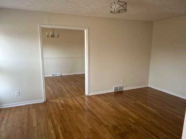 unfurnished room featuring visible vents, a textured ceiling, wood finished floors, baseboards, and a chandelier