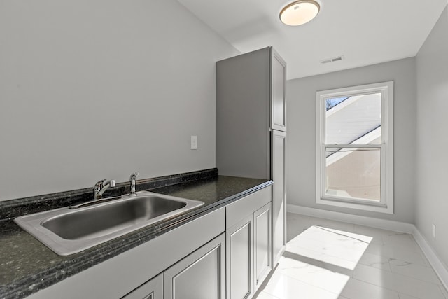 kitchen with visible vents, marble finish floor, a sink, dark stone counters, and baseboards