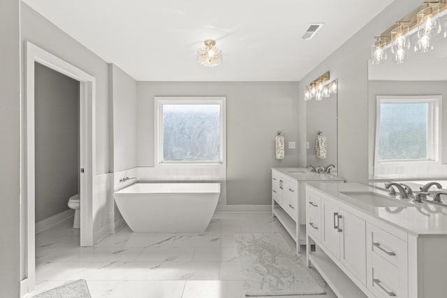 bathroom with marble finish floor, a freestanding bath, vanity, and toilet