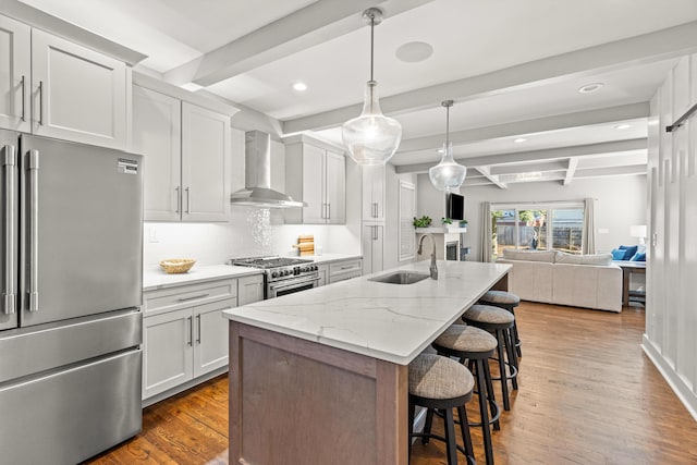 kitchen with a breakfast bar, a sink, wall chimney range hood, high quality appliances, and open floor plan