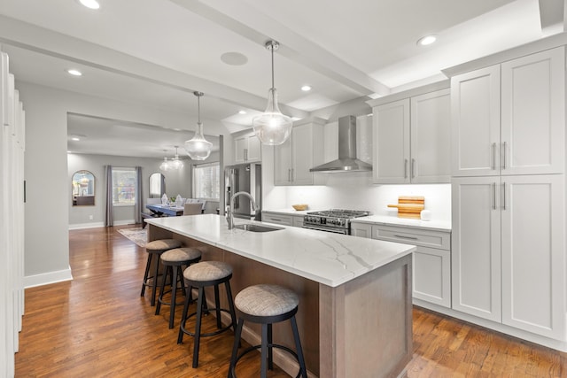 kitchen with beamed ceiling, an island with sink, a sink, wall chimney exhaust hood, and high end appliances