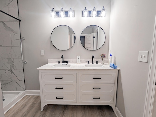 bathroom featuring double vanity, wood finished floors, a tile shower, and a sink