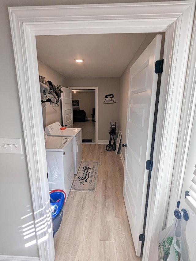 clothes washing area featuring laundry area, separate washer and dryer, baseboards, and light wood finished floors