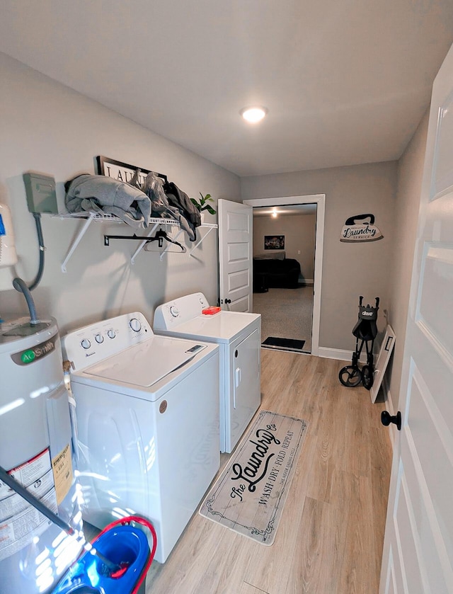 clothes washing area with washing machine and clothes dryer, baseboards, light wood-type flooring, water heater, and laundry area