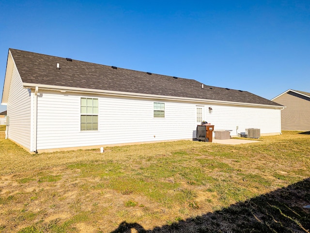 back of property with a yard, cooling unit, and a shingled roof