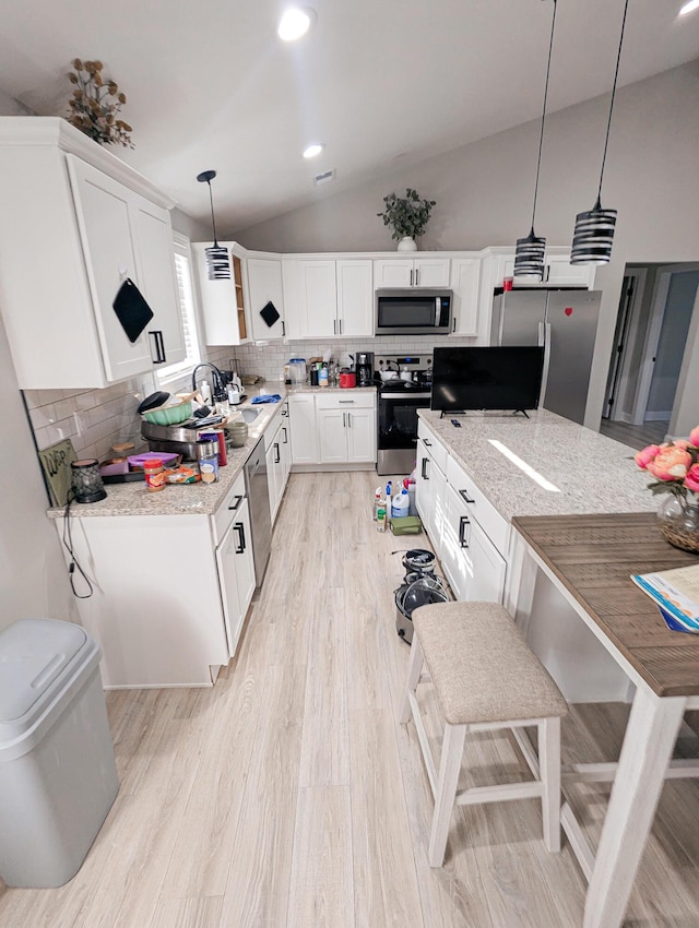 kitchen with light stone countertops, light wood finished floors, stainless steel appliances, vaulted ceiling, and tasteful backsplash