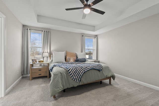 bedroom featuring a tray ceiling, light carpet, and baseboards