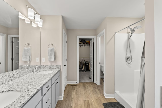 full bath featuring a walk in closet, a stall shower, a sink, wood finished floors, and double vanity