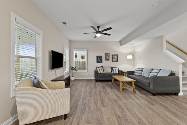 living room featuring wood finished floors, a ceiling fan, visible vents, baseboards, and stairs