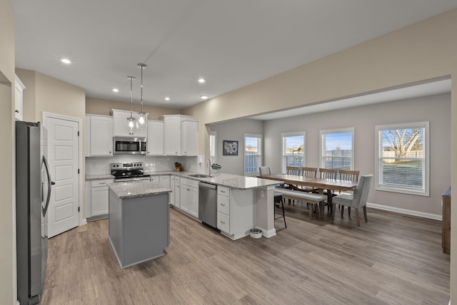 kitchen with light wood-type flooring, tasteful backsplash, appliances with stainless steel finishes, a peninsula, and white cabinets