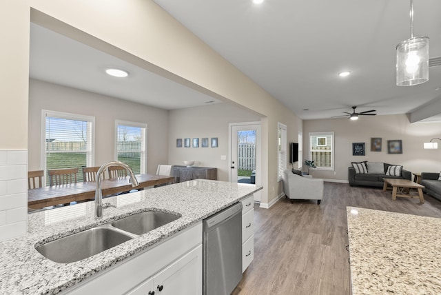 kitchen featuring light stone counters, a sink, white cabinets, stainless steel dishwasher, and open floor plan