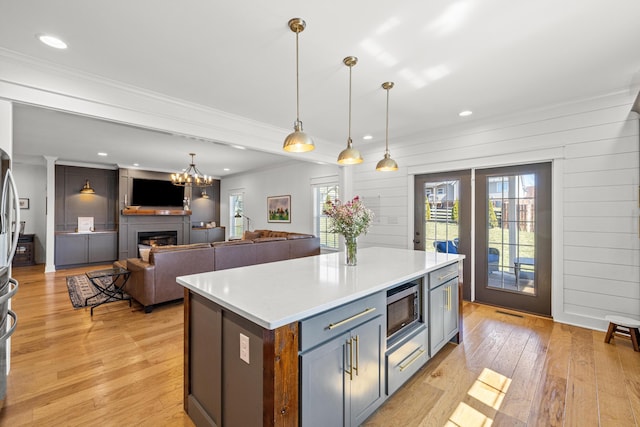 kitchen featuring light wood-type flooring, stainless steel microwave, a warm lit fireplace, light countertops, and hanging light fixtures