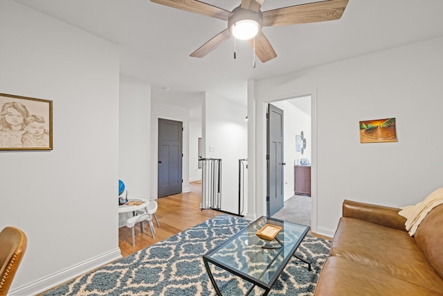 living room with light wood-type flooring, baseboards, and ceiling fan