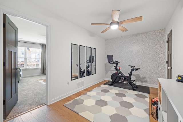 workout area featuring light wood finished floors, visible vents, wallpapered walls, an accent wall, and baseboards