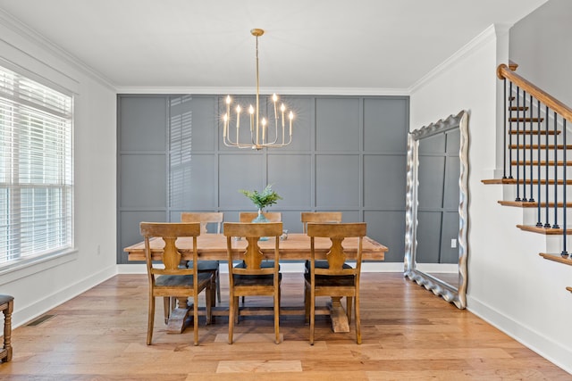 dining space with light wood-type flooring, an inviting chandelier, crown molding, a decorative wall, and stairs