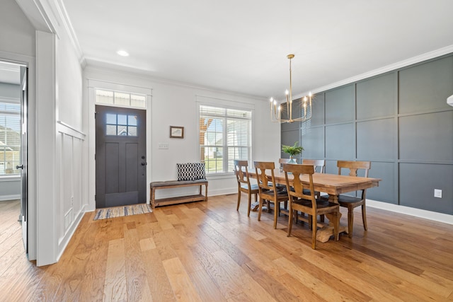 dining space featuring baseboards, light wood finished floors, an inviting chandelier, crown molding, and a decorative wall