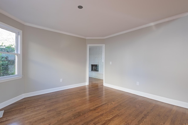 unfurnished room featuring a brick fireplace, wood finished floors, baseboards, and ornamental molding