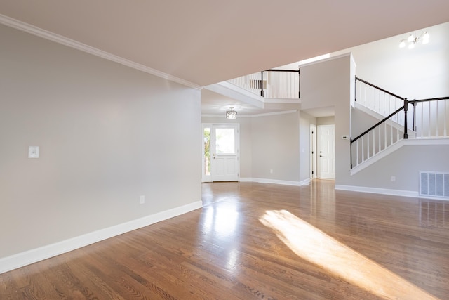 unfurnished living room featuring wood finished floors, visible vents, baseboards, ornamental molding, and stairs