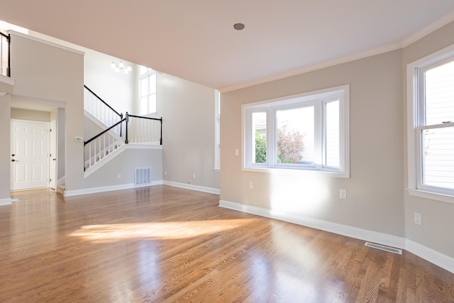 unfurnished living room with visible vents, wood finished floors, crown molding, baseboards, and stairs