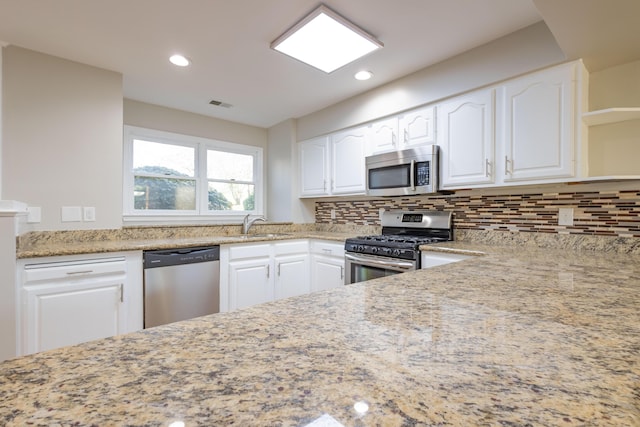 kitchen featuring light stone counters, visible vents, stainless steel appliances, decorative backsplash, and white cabinetry